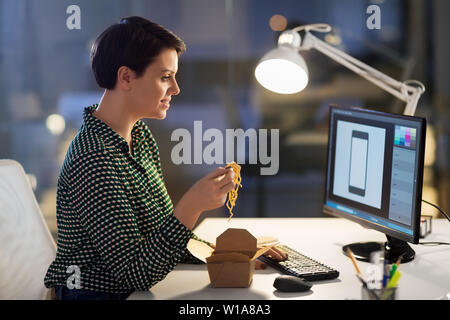 female designer eating and working at night office Stock Photo