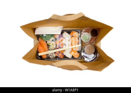 Sushi to go concept. Top view of takeaway box with sushi rolls and various sauce cups in brown paper bag. Isolated on white, studio shot. Stock Photo