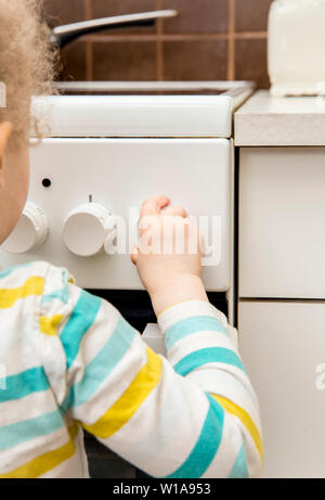 Close up view of unattended child playing and turning kitchen stove knobs alone in kitchen. Fire hazard in home concept. Stock Photo