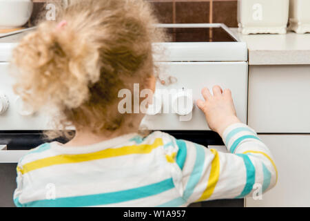 Close up view of unattended child playing and turning kitchen stove knobs alone in kitchen. Fire hazard in home concept. Stock Photo