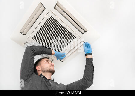 Handsome young technician repairing air conditioner. Installing air conditioning system. Stock Photo