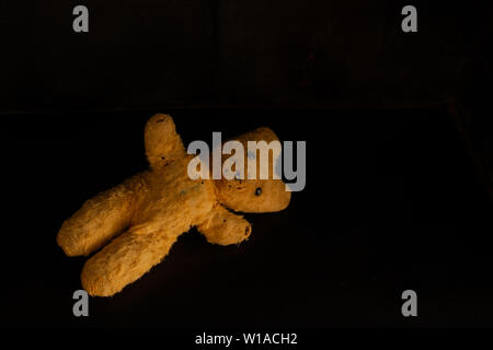 An abandoned and battered old teddy bear from the 1960s lies on a black background. Includes space for copy Stock Photo