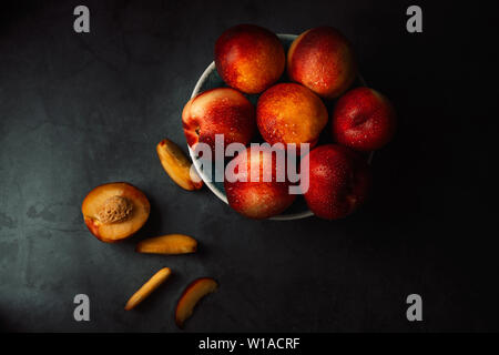 Still life of fresh delicious sweet nectarines with droplets of water in a bowl on dark background. Low key. Top view. Stock Photo