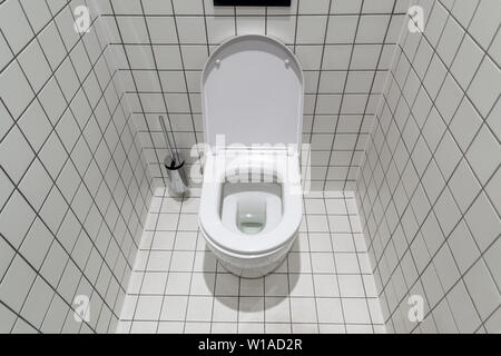 New clean toilet, with modern design and white ceramic toilet bowl against light tiles. Stock Photo