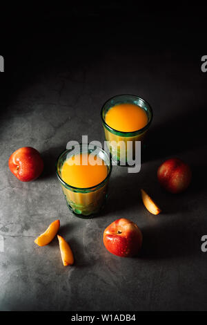 Still life of fresh delicious sweet nectarines with droplets of water and juice in turquoise vintage glasses on dark background. Low key. Stock Photo