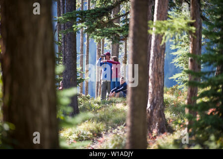 Man looking through binoculars while standing next to his wife and son in the middle of a wooded area. Stock Photo