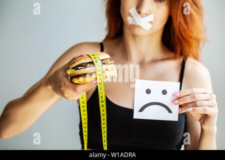 Diet. Portrait woman wants to eat a Burger but stuck skochem mouth, the concept of diet, junk food, willpower in nutrition. Stock Photo