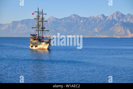 Tourist tour boat in ocean entering the harbour of Antalya.  Sunny morning with light on boat in front of mountain range to the sea. Antalya, Turkey - Stock Photo