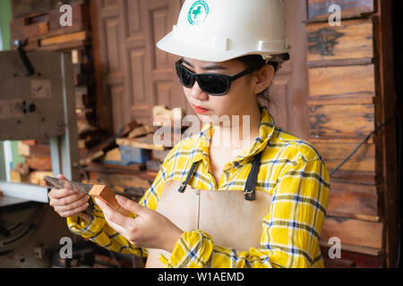 Woman holding ruler and pencil while making marks on the wood at the table in the workshop Stock Photo