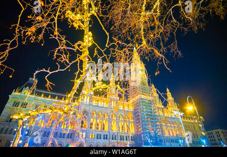 The view on bright illumination of the Rathaus (City Hall) of Vienna among branches of park's trees, decorated with celebration lamps, Vienna, Austria Stock Photo