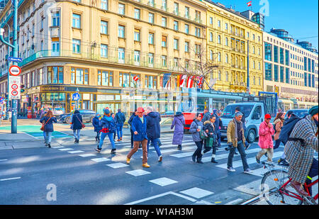 VIENNA, AUSTRIA - FEBRUARY 18, 2019: Locals and tourists crossing the busy Ringstrasse on the crosswalk next to the Opera House, on February 18 in Vie Stock Photo
