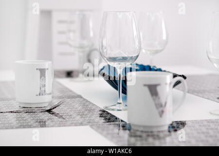 On a white kitchen dining table on place mat tea cups close up focus on empty transparent clear wine glass at the cozy modern room Stock Photo