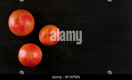 Top down view, three pink grapefruits on black marble board, banner with space for text at right side. Stock Photo