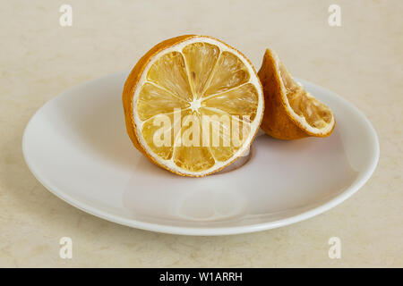 Lemon dried in the fridge. Stale citrus on a white saucer. Foods forgotten in the home refrigerator. Stock Photo