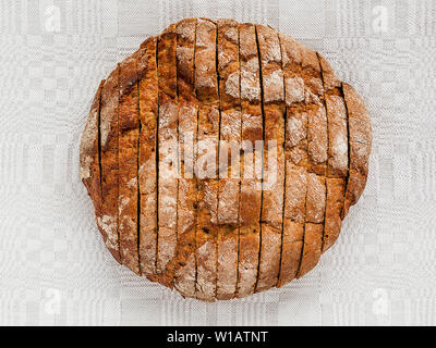 Sliced round loaf of rye bread with an appetizing crispy brown crust on a gray linen tablecloth. Tasty, usefull and nutritious. Directly above view. Stock Photo