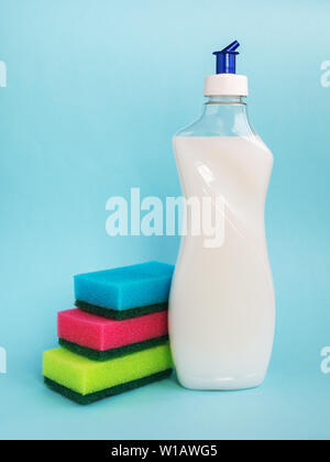 Bottle with white dishwashing liquid and three foam sponges of different colours on a blue background. Kitchen chemicals.Household detergent. Stock Photo