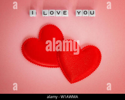 Two red valentine hearts and the inscription I love You made of white alfphabet cubes on pastel pink background. Concept love, Valentine's day. Flat l Stock Photo