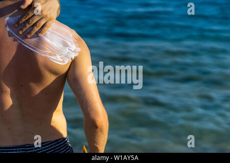 young man with wave-formed suncream on his shoulder standing at the beach, looking over the sea Stock Photo