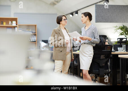 Side view portrait of two contemporary businesswomen discussing work plans while standing in office, copy space Stock Photo