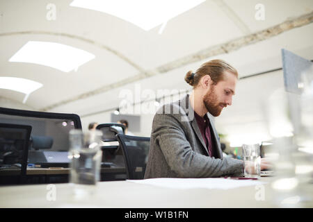 Side view portrait of handsome bearded businessman using laptop while working in open space office Stock Photo