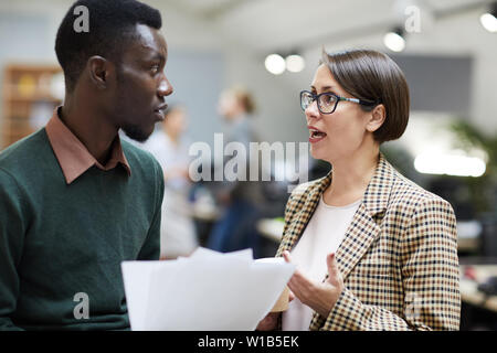 Side view portrait of female business manager talking to to African-American colleague while working in office, copy space Stock Photo