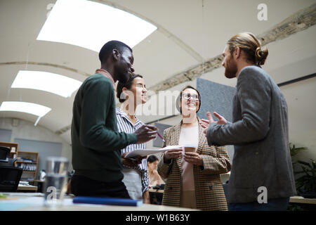 Low angle view at multi -ethnic group of business people laughing happily while chatting during coffee break in office, copy space Stock Photo