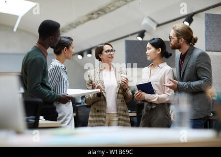 Portrait of successful businesswoman talking to employees while standing in modern office, copy space Stock Photo