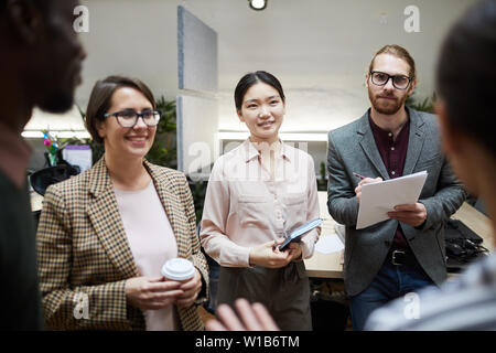 Waist up portrait of multi-ethnic group of business people listening to colleague and taking notes while discussing project in office Stock Photo