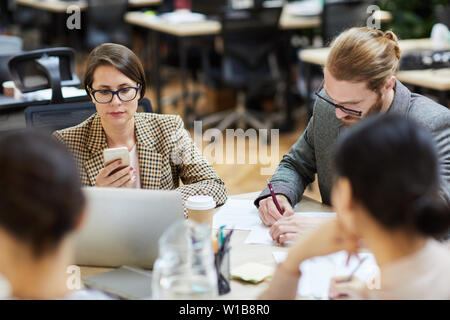 Portrait of modern businesswoman using smartphone during work meeting in office, copy space Stock Photo