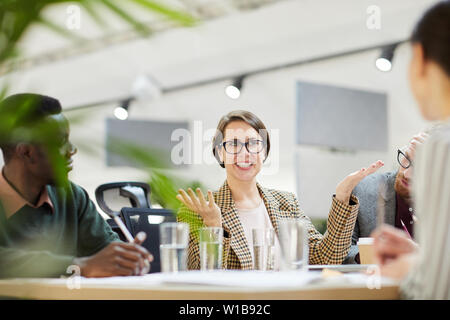 Portrait of cheerful businesswoman wearing glasses gesturing actively during meeting in office, copy space Stock Photo