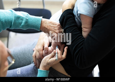 Real baby being vaccinated with a syringe in the thigh by a pediatrician doctor to avoid the spread of diseases. Stock Photo