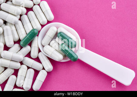 Plastic spoon and green and white pills on pink background. Stock Photo