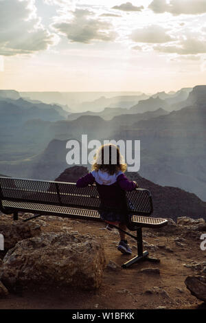 Back Caucasian, curly haired tourist woman watching sunset from a bench in Desert View, Grand Canyon National Park, Arizona, USA