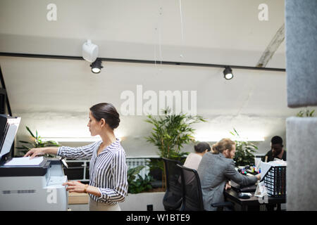 Side view portrait of young businesswoman scanning documents while working in office, copy space Stock Photo