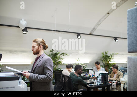 Side view portrait of handsome businessman printing documents while working in office, copy space Stock Photo