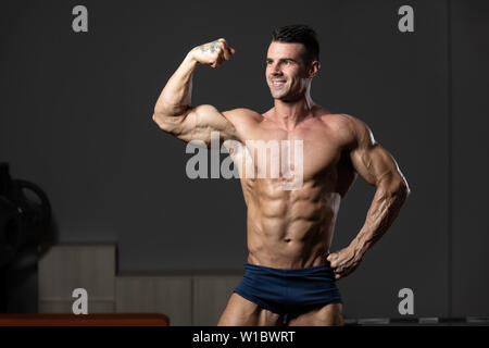 Young Man Standing Strong In The Gym And Flexing Muscles - Muscular Athletic  Bodybuilder Fitness Model Posing After Exercises Stock Photo - Alamy