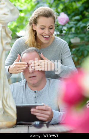 woman surprising man by covering his eyes from behind Stock Photo