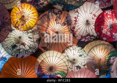 Multi colored chinese umbrellas hanging on a wall illuminated at night Stock Photo