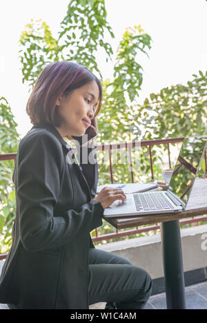 Woman wearing black suit working on laptop and using cellphone Stock Photo