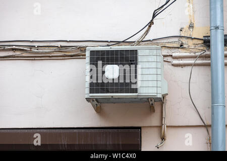 White air conditioning on the old wall of the house with the old wires of communication on the plastic drain pipe above the window. Cooling and comfor Stock Photo