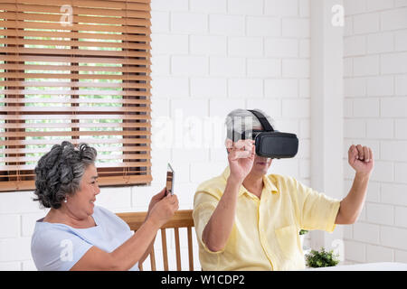 Asian senior couple play virtual realtiy glasses headset and tablet watching vr video and  have fun together in living room at home.senior with techno Stock Photo