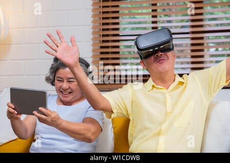 Asian senior couple play virtual realtiy glasses headset and tablet watching vr video and  have fun together in living room at home.senior with techno Stock Photo