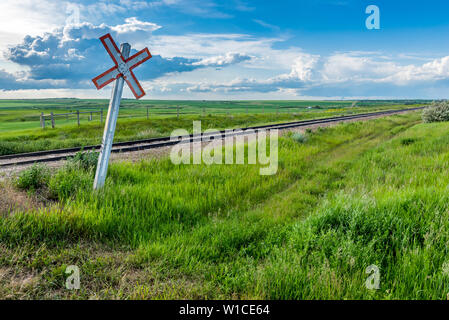 Prairie railway crossing sign and tracks with storm clouds on the horizon in Saskatchewan, Canada Stock Photo