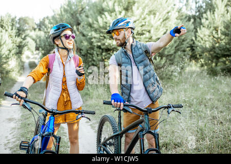 Young couple traveling with mountain bicycles in the forest, man showing with hand on the way forward Stock Photo