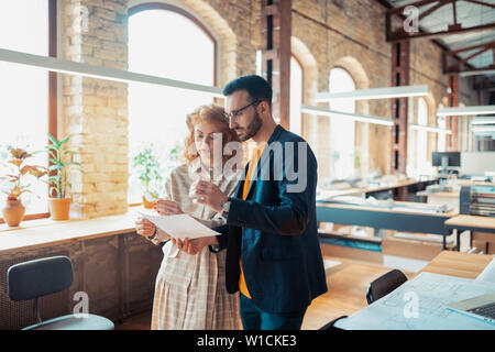 Boss assisting. Handsome bearded boss assisting his interior designer while making sketches Stock Photo