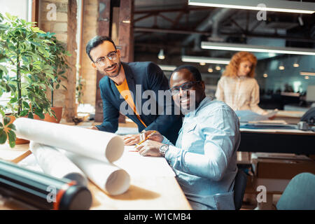 With smart colleague. Dark-skinned interior designer smiling while working with smart colleague Stock Photo
