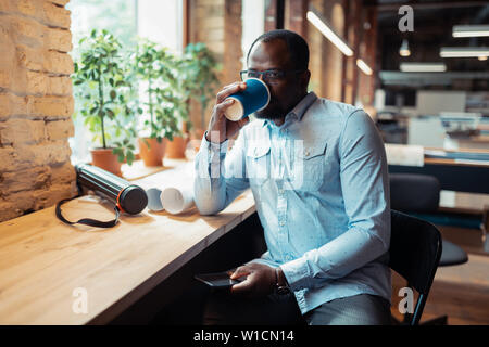 Drinking coffee. Dark-skinned mature interior designer drinking coffee sitting near window Stock Photo