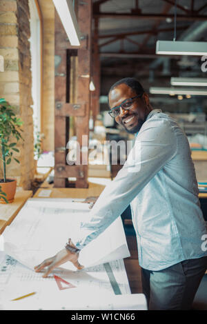 Designer smiling. Dark-skinned interior designer smiling while working hard and making sketches Stock Photo