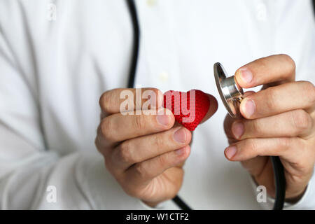 Doctor with stethoscope and red knitted heart in hand. Concept of cardiologist, heart diseases, diagnosis, blood pressure, medical exam Stock Photo