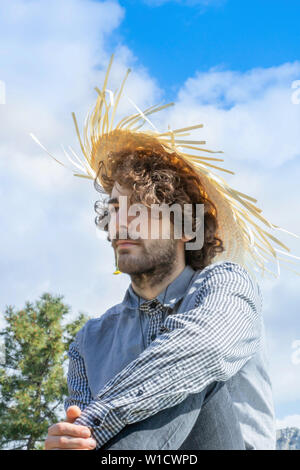 Young adult man looking away, brown curly hair with a West Indian straw hat on his head Stock Photo